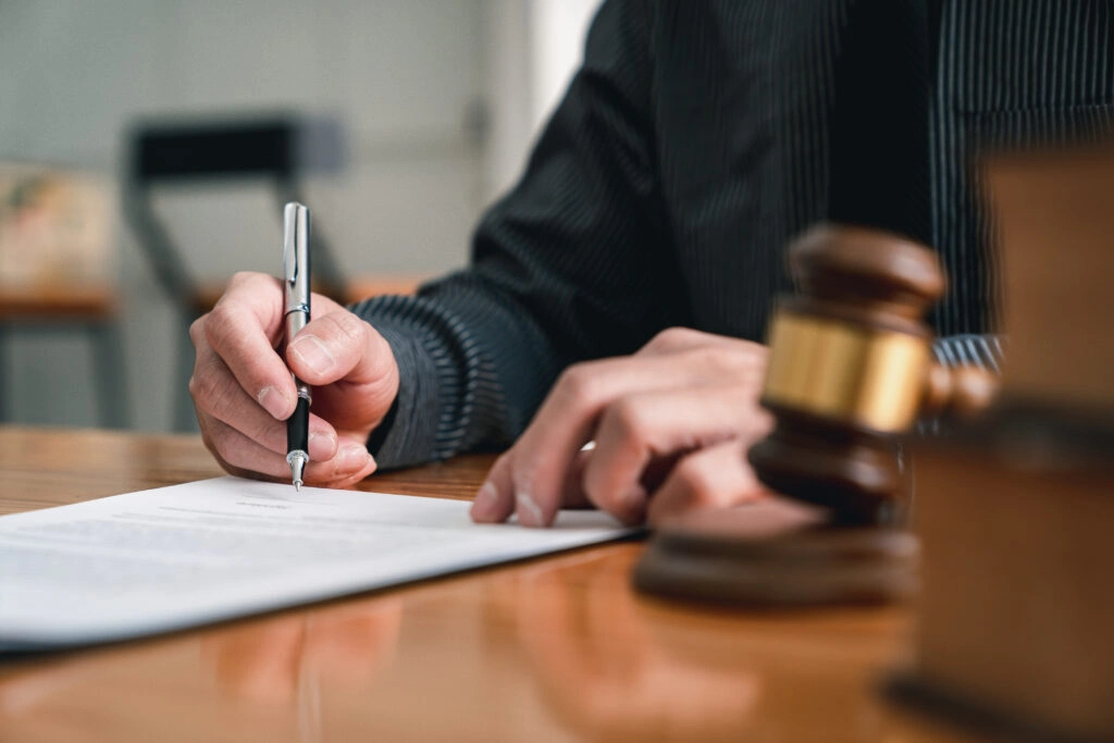 Person signing a document beside a gavel